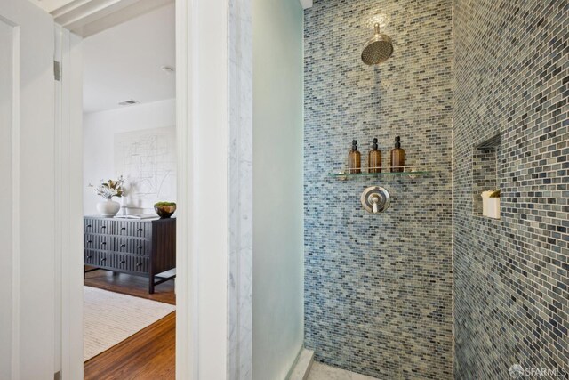 bathroom with tiled shower, wood finished floors, and visible vents