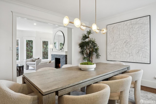 dining space featuring a warm lit fireplace, baseboards, wood finished floors, and crown molding