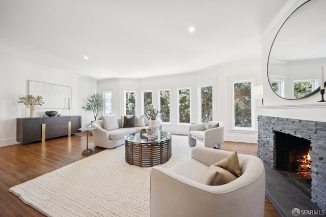 living area featuring dark wood-type flooring, a healthy amount of sunlight, a fireplace, and ornamental molding