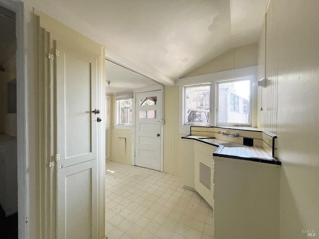 kitchen with tile countertops, vaulted ceiling, and white cabinetry