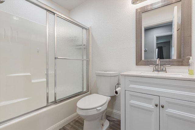 bathroom featuring a textured wall, toilet, shower / bath combination with glass door, wood finished floors, and vanity