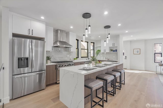 kitchen featuring wall chimney exhaust hood, light stone counters, a center island, stainless steel appliances, and white cabinets