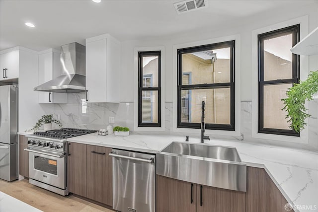 kitchen featuring light stone countertops, white cabinetry, appliances with stainless steel finishes, and wall chimney exhaust hood