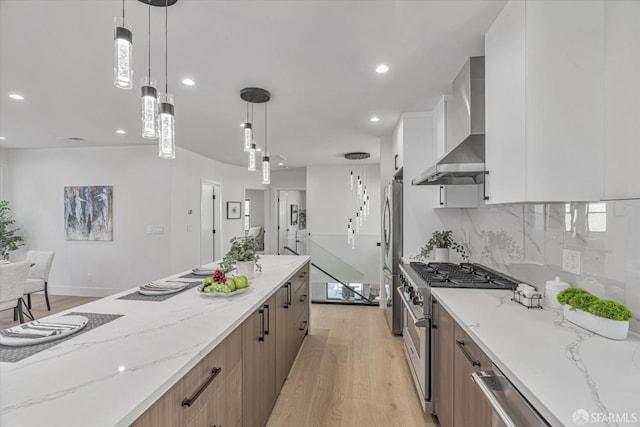 kitchen featuring appliances with stainless steel finishes, white cabinetry, light stone countertops, decorative light fixtures, and wall chimney exhaust hood