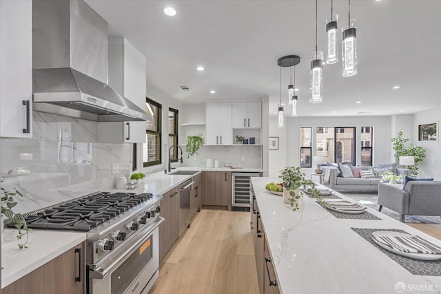 kitchen featuring appliances with stainless steel finishes, light stone counters, white cabinets, beverage cooler, and wall chimney exhaust hood