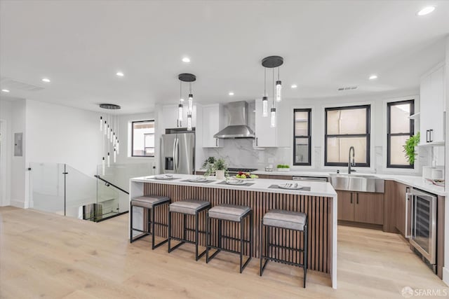 kitchen with a kitchen island, pendant lighting, white cabinetry, stainless steel fridge with ice dispenser, and wall chimney range hood