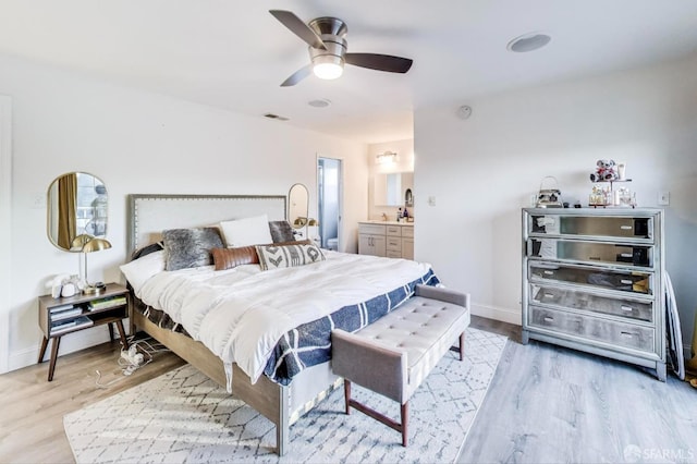 bedroom featuring ceiling fan, ensuite bathroom, visible vents, baseboards, and light wood-style floors