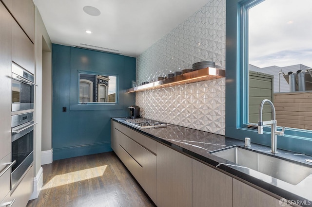 kitchen featuring appliances with stainless steel finishes, dark stone countertops, tasteful backsplash, light hardwood / wood-style flooring, and sink