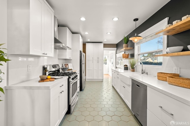 kitchen featuring sink, white cabinets, pendant lighting, stainless steel appliances, and wall chimney range hood