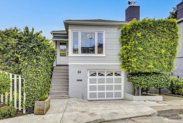 view of front facade featuring driveway, a chimney, an attached garage, and stucco siding