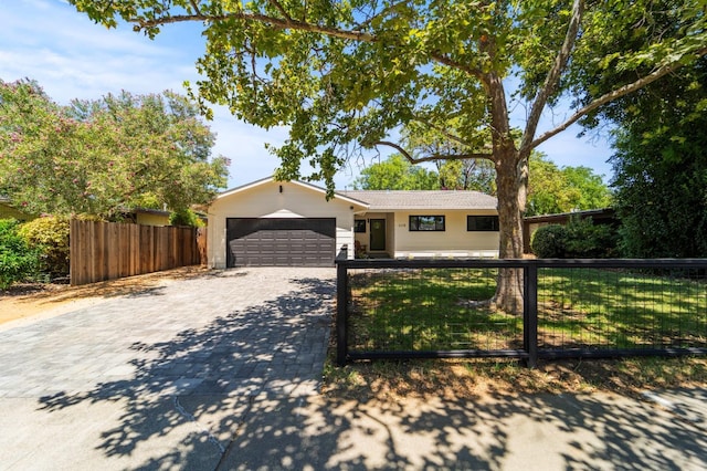 ranch-style home featuring an attached garage, a fenced front yard, and decorative driveway