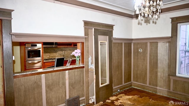 interior space featuring ornamental molding, stainless steel oven, wood-type flooring, and an inviting chandelier