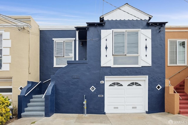 view of front facade with a garage, concrete driveway, stairs, and stucco siding