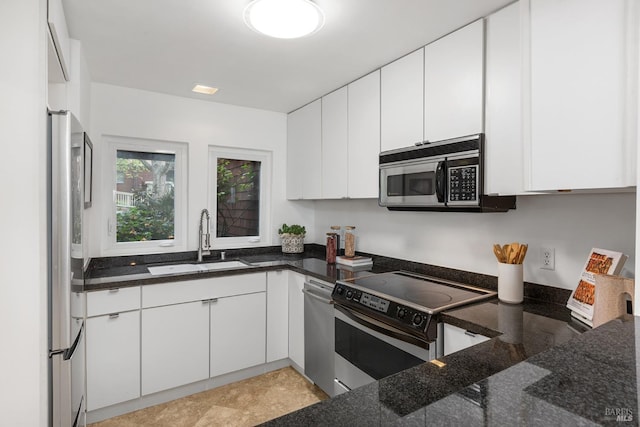 kitchen featuring appliances with stainless steel finishes, dark stone counters, white cabinets, and a sink