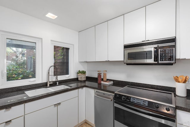 kitchen featuring appliances with stainless steel finishes, white cabinetry, dark stone countertops, and a sink