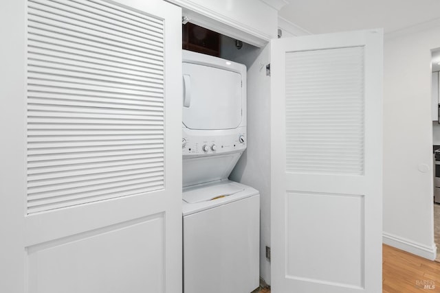 laundry area with baseboards, stacked washer and clothes dryer, light wood-style floors, and laundry area