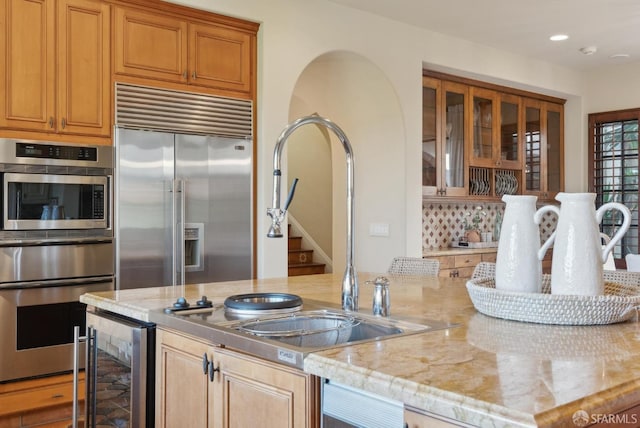 kitchen with light stone counters, beverage cooler, appliances with stainless steel finishes, and a sink