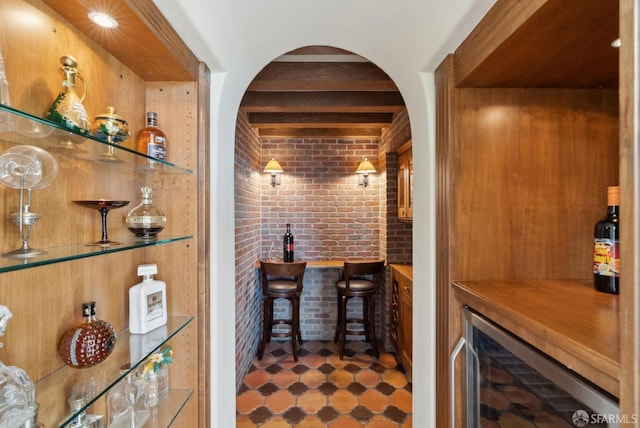 wine room with beverage cooler, brick wall, beam ceiling, arched walkways, and a dry bar