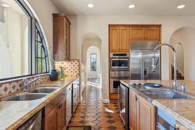 kitchen featuring beverage cooler, arched walkways, a sink, stainless steel appliances, and tasteful backsplash