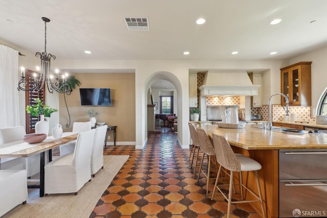 kitchen featuring tasteful backsplash, visible vents, a breakfast bar, custom range hood, and arched walkways