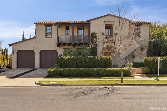 mediterranean / spanish-style home featuring concrete driveway, a tiled roof, a balcony, and stucco siding