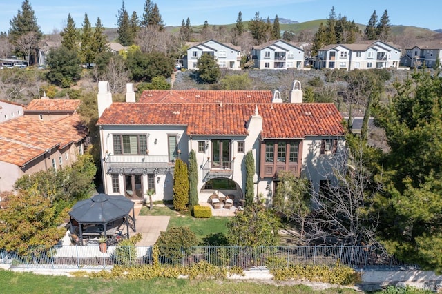 back of property featuring a tiled roof, a chimney, a fenced backyard, a balcony, and a patio