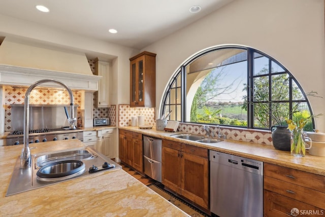 kitchen with glass insert cabinets, light countertops, decorative backsplash, stainless steel dishwasher, and a sink