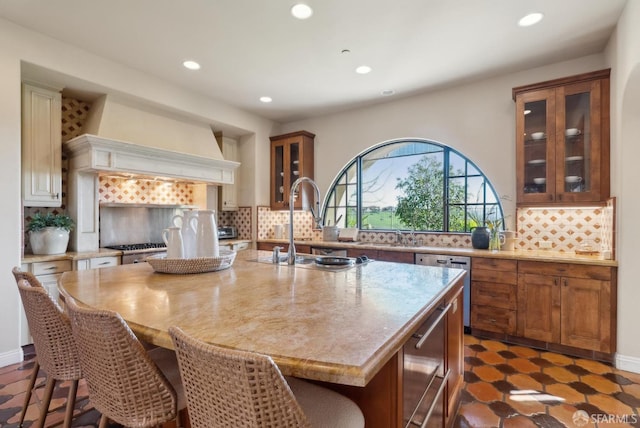 kitchen with tasteful backsplash, an island with sink, custom range hood, recessed lighting, and stainless steel dishwasher