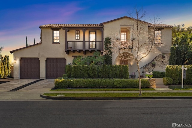 mediterranean / spanish home featuring stucco siding, concrete driveway, a garage, a balcony, and a tiled roof