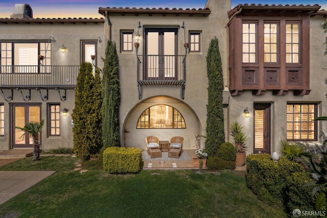 rear view of house featuring french doors, a balcony, a yard, and stucco siding