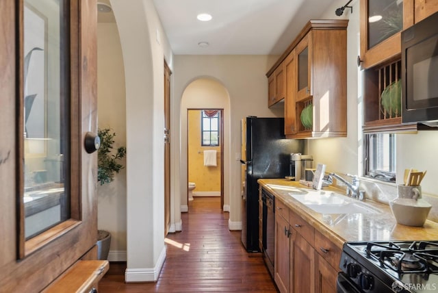 kitchen featuring black appliances, a sink, arched walkways, brown cabinetry, and light countertops