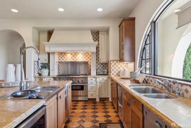 kitchen with tasteful backsplash, premium range hood, appliances with stainless steel finishes, and a sink