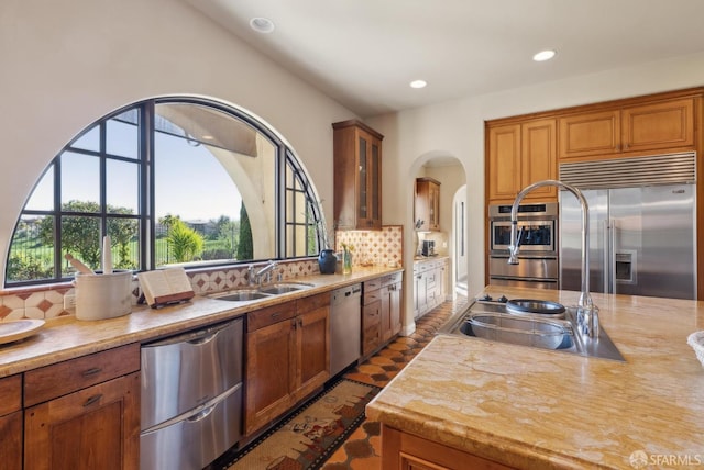 kitchen with backsplash, light countertops, arched walkways, stainless steel appliances, and a sink