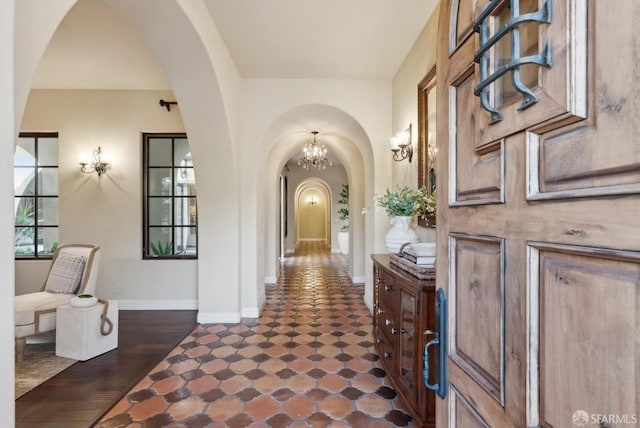 entryway with arched walkways, a notable chandelier, baseboards, and dark wood-style floors