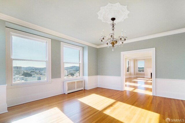 spare room with ornamental molding, hardwood / wood-style flooring, a chandelier, and radiator heating unit