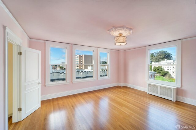 unfurnished room featuring radiator, light wood-type flooring, crown molding, and a healthy amount of sunlight