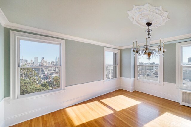 unfurnished dining area featuring ornamental molding, hardwood / wood-style flooring, a chandelier, and radiator heating unit