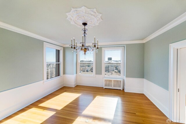 unfurnished dining area featuring hardwood / wood-style flooring, crown molding, a chandelier, and radiator heating unit