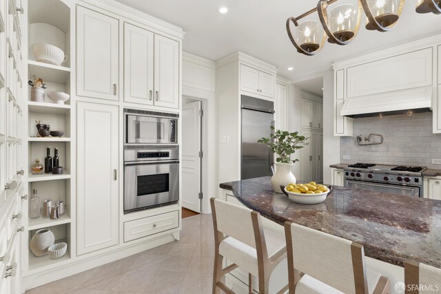 kitchen featuring a kitchen breakfast bar, white cabinets, built in appliances, premium range hood, and a chandelier