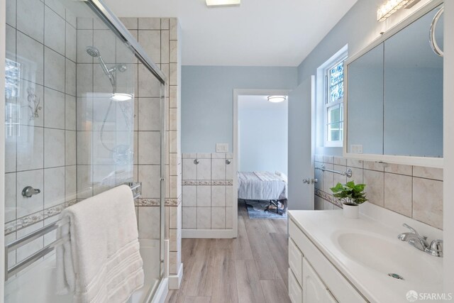 ensuite bathroom with a shower stall, wood finished floors, vanity, and tile walls