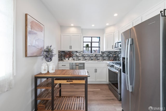 kitchen featuring tasteful backsplash, white cabinets, appliances with stainless steel finishes, light countertops, and a sink