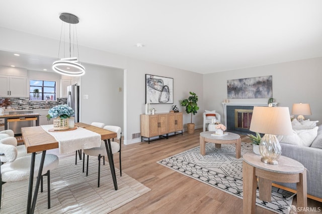 living area featuring light wood-style floors, baseboards, a glass covered fireplace, and recessed lighting