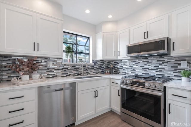 kitchen featuring light stone counters, backsplash, white cabinets, stainless steel appliances, and a sink