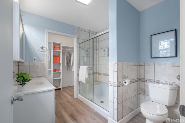 bathroom with toilet, tile walls, a shower stall, and wood finished floors
