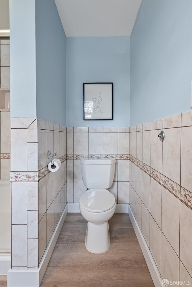 bathroom featuring toilet, wood finished floors, a wainscoted wall, and tile walls