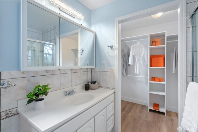 full bath featuring tile walls, an enclosed shower, a walk in closet, vanity, and wood finished floors