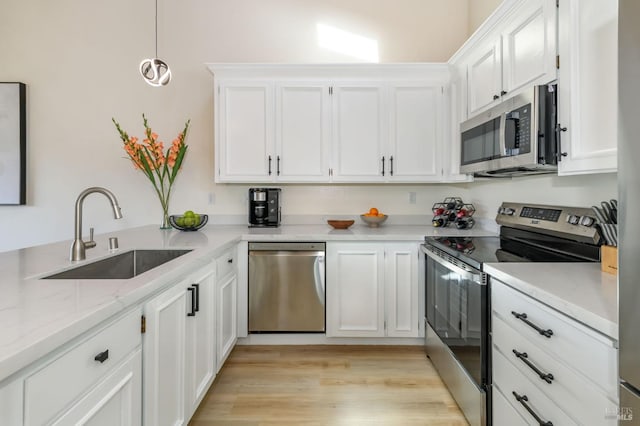 kitchen with light stone countertops, light wood-style flooring, a sink, stainless steel appliances, and white cabinetry