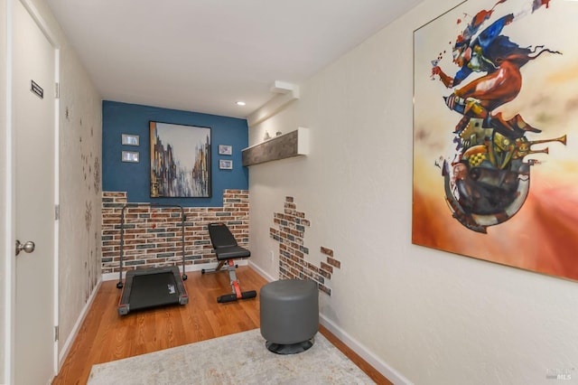 exercise area featuring brick wall, baseboards, and wood finished floors