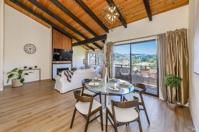 dining space featuring beamed ceiling, wooden ceiling, a fireplace, and light wood finished floors