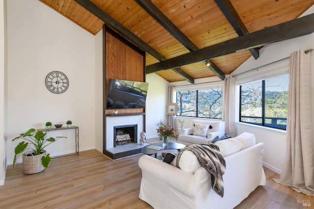 living area with a fireplace with raised hearth, vaulted ceiling with beams, baseboards, wood ceiling, and light wood-style floors